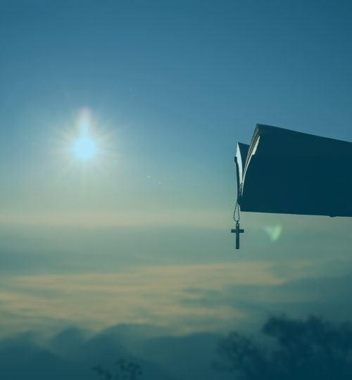 Silhouette of human hand holding bible and cross, the background is the sunrise., Concept for Christian, Christianity, Catholic religion, divine, heavenly, celestial or god.